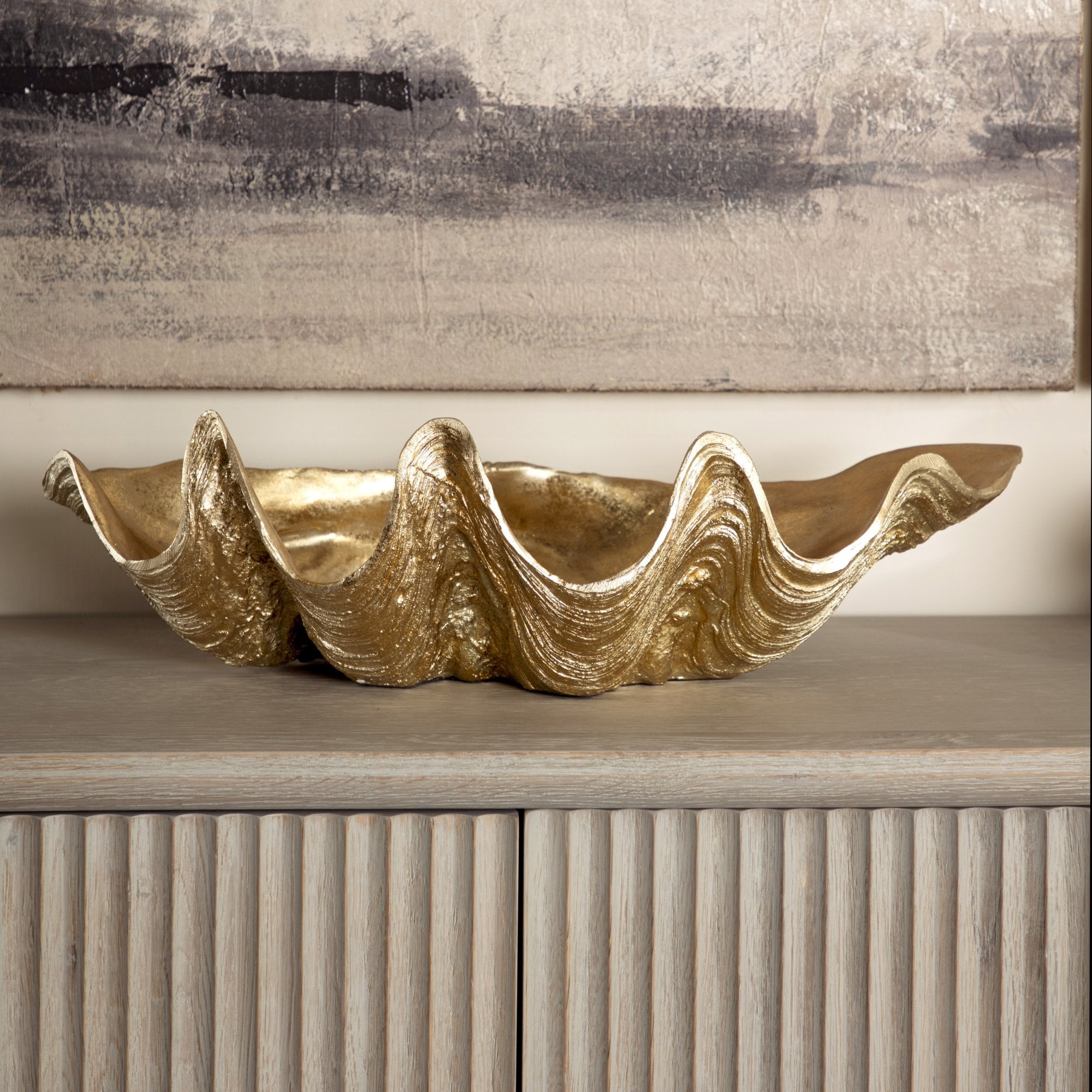 Gold shell-shaped decorative piece on a wooden surface with a textured wall background