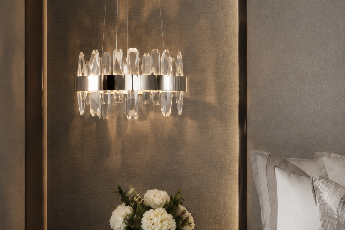 A modern multi-light chandelier with clear crystal droplets and silver-toned metal accents, hanging in a luxury bedroom above a dark wood nightstand with a vase of white flowers.