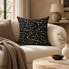 A square throw pillow with a black and cream abstract organic pattern, styled on a cream bouclé sofa in a warm, neutral-toned living room.
